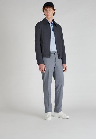 Chaqueta gris oscura con cuello, camisa azul clara, pantalones grises con estampado y zapatillas blancas, sobre un fondo neutro.