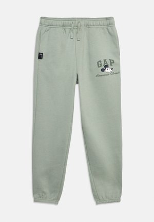 Pantalon de survêtement vert clair avec taille et poignets élastiques, poches avant, et un graphisme de Mickey Mouse avec le texte "GAP American Classic" sur la cuisse.