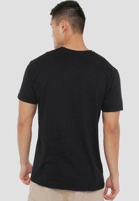 Black cotton t-shirt with a classic crew neck and short sleeves, shown from the back. Smooth texture and regular fit design.
