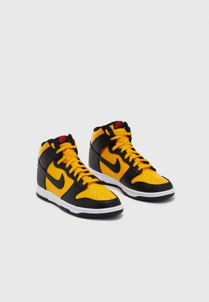 Czarno-żółte buty Nike typu high-top z czerwonymi akcentami logo, białą środkową podeszwą i żółtymi sznurowadłami, ustawione obok siebie na jednolitym tle.