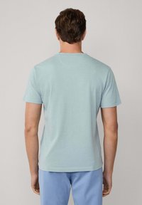 Světle modré pruhované tričko s krátkými rukávy a kulatým výstřihem, vyrobené z měkké tkaniny. Pohled ze zad ukazuje jemnou strukturu a uvolněný střih.