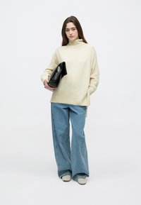 Kremo spalvos, per didelis megztinis su aukštu kaklu, derinamas su plačiomis šviesiai mėlynomis džinsais. Laiko juodą, struktūruotą delninę rankinę.