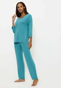 Completo da loungewear turchese composto da una maglia a V con maniche a tre quarti e pantaloni dritti coordinati, realizzato in un tessuto morbido e liscio.