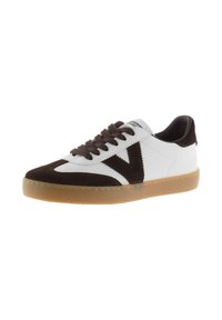 Zapatillas de ante blancas y marrones con cordones planos, suela de goma y un diseño en forma de V en los laterales. El contraste de colores resalta los materiales.