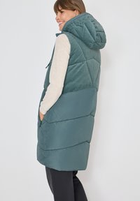 Gepolsterte Weste mit Kapuze in Tealfarbe, gestepptem Design und seitlichen Taschen. Hergestellt aus Mischgewebe mit glatten und gerippten Abschnitten.
