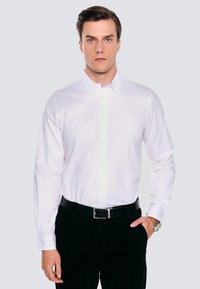 Biała koszula z długim rękawem, z klasycznym kołnierzykiem, noszona z czarnymi spodniami i czarnym paskiem; gładka tekstura, brak widocznych wzorów lub akcentów.