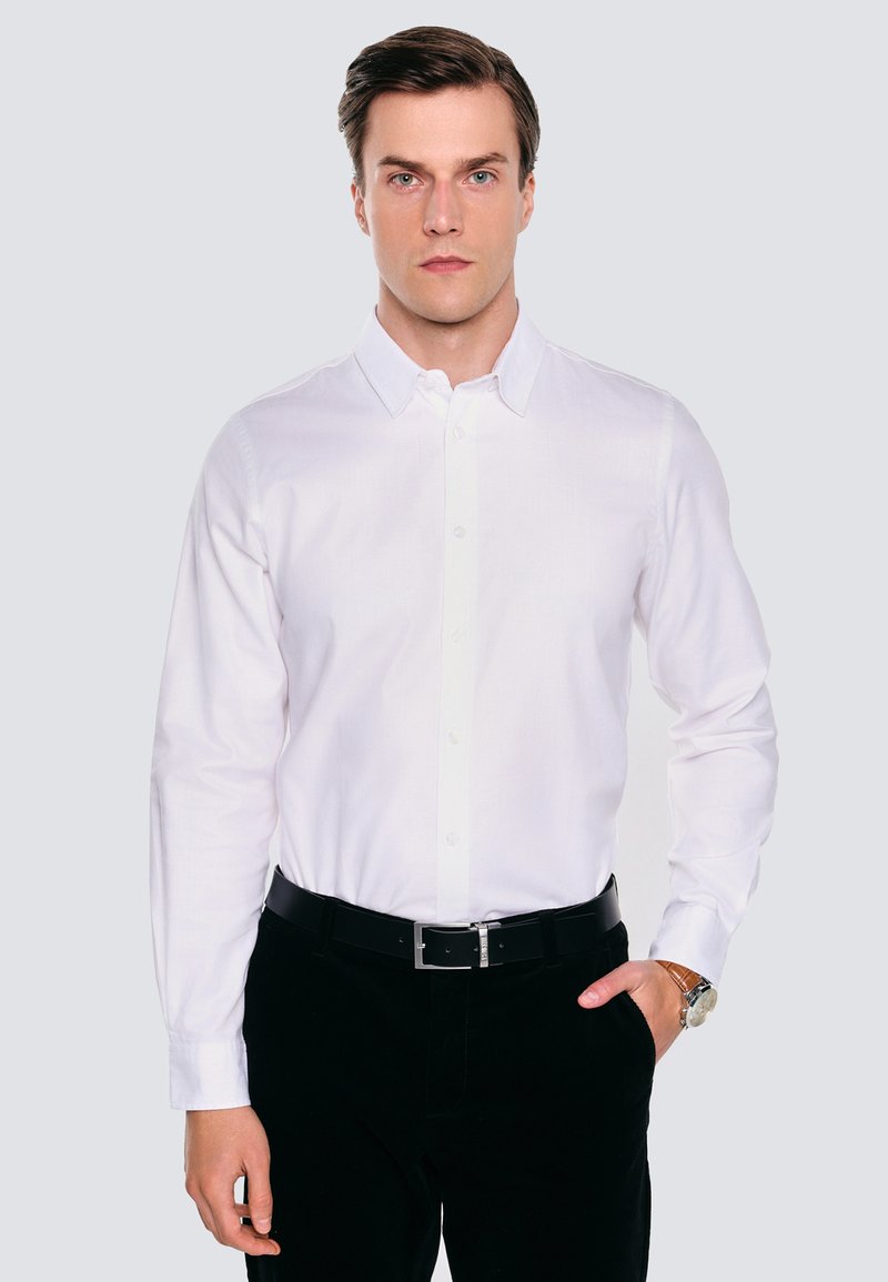 Biała koszula z długim rękawem, z klasycznym kołnierzykiem, noszona z czarnymi spodniami i czarnym paskiem; gładka tekstura, brak widocznych wzorów lub akcentów.