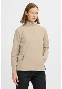 Beige fleece pullover met een hoge kraag, voorkant met rits en zijzakken. Zachte textuur en een ontspannen pasvorm, ideaal voor het laagjes dragen.