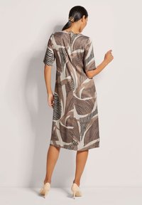 Braun und cremedurchzogenes Kleid mit kurzen Ärmeln, das abstrakte Designs und einen geraden Schnitt aufweist, kombiniert mit hellen Schuhen.