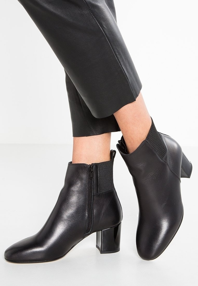 Bottines en cuir noir avec un bout pointu, une fermeture éclair sur le côté et un accent côtelé à la cheville ; finition avec un talon bloc brillant.