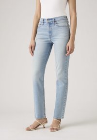 Lichtblauwe denim jeans met rechte pijpen, mid-rise, met een verweerde wassing. Voorzien van een klassieke vijfzakkenontwerp en ceintuurlussen. Gecombineerd met beige sandalen met hak.