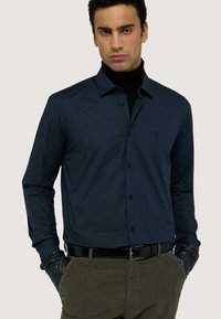 Camicia a maniche lunghe blu navy realizzata in tessuto liscio, con chiusura a bottoni frontale, colletto classico e logo del marchio discreto sul petto.