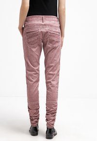 Rosa, åtsittande jeans med en slät yta, avslappnade mudd och två bakfickor. Midjan har sömnadsdetaljer.