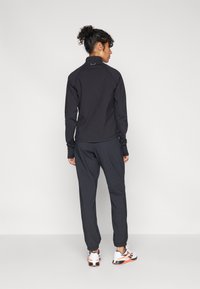 Sort sports-top med høj krave, parret med sorte joggingbukser. Bemærkelsesværdige detaljer inkluderer tommelhuller ved ærmerne og hvide sneakers.