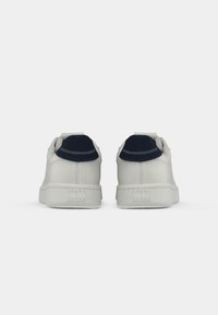 Witte sneakers van glad leer, marineblauwe accenten bij de hiel, platte zool en een reliëf merknaam op de achterkant.