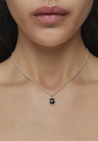 Collar de cadena de plata con un colgante negro en una forma geométrica única, sobre piel desnuda, resaltando su diseño minimalista.