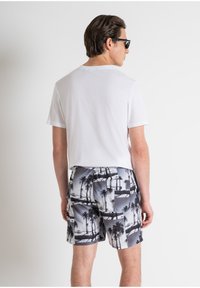 Camiseta blanca de algodón para hombre y bañador gris con un estampado de palmera y escena de playa. El bañador cuenta con una cinturilla elástica.