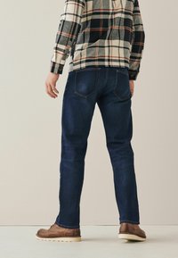Sötétkék, slim fit farmerek, barna bőrcipővel párosítva. A kockás flaneling fekete, fehér és narancssárga csíkokkal rendelkezik.