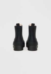 Zwarte enkelboots van soepel leer met ribbelaccenten op de hak, voorzien van een trekhaak en zachte binnenvoering. Chunky, gestructureerde zolen.