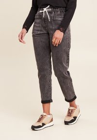Grijze denim joggers met een elastische tailleband en witte koord, voorzien van zijzakken en omgeslagen boorden, gecombineerd met beige en zwarte sneakers.