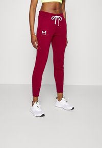 Bordeauxrote Sweatpants aus Baumwollmischung mit schmalem Schnitt, weißem Kordelzug und Under Armour-Logo auf dem linken Oberschenkel. Kombiniert mit weißen Turnschuhen.