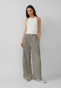 Witte mouwloze top met rhinestone-accenten, gecombineerd met lichtgrijze plooipantalon met wijde pijpen en metallic zilveren ballerina's.