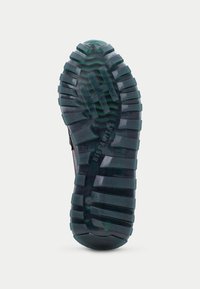 Semelle de chaussure avec des rainures profondes et des crampons, en caoutchouc de couleur vert foncé. Présente une surface texturée pour une meilleure traction et stabilité.