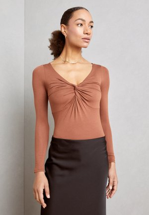 Long-sleeve, rust-colored bodysuit with a V-neck and gathered detailing at the center, paired with a black satin skirt. Smooth texture.