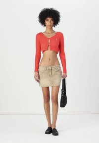 Coral cropped sweater with button closure, paired with a beige denim mini skirt. Includes a black shoulder bag and black loafers.