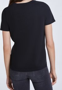 Camiseta negra de manga corta hecha de una tela suave, con un cuello redondo clásico y un corte relajado, combinada con pantalones vaqueros oscuros de denim.