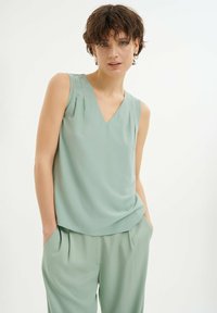 Top senza maniche di un verde chiaro, con scollatura a V. Realizzato in tessuto morbido, presenta una leggera drappeggiatura sulle spalle e una vestibilità comoda.
