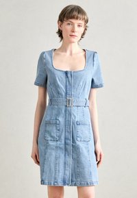 Denimkleit lühikeste varrukatega, ruudu kujuline kaelus, keskel asuv lukk ja kaks eesmist taskut. Omab kangast vööd ruudukujulise pandlaga.