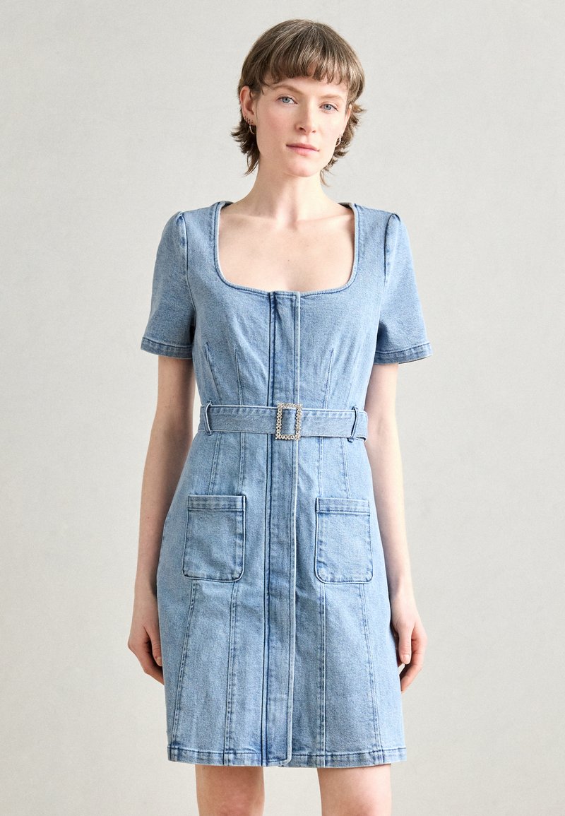 Denimkleit lühikeste varrukatega, ruudu kujuline kaelus, keskel asuv lukk ja kaks eesmist taskut. Omab kangast vööd ruudukujulise pandlaga.