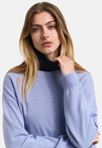 Hellblauer Pullover aus weichem Stoff, mit hohem schwarzen Rollkragen, lockerer Passform und Rippbündchen, entworfen für Komfort.