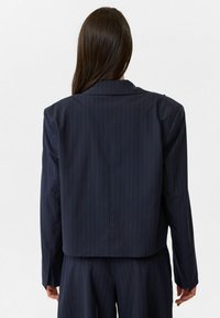 Marineblauwe pinstripe blazer met een relaxte pasvorm, gestructureerde schouders en lange mouwen. De stof heeft een gladde en lichte textuur.