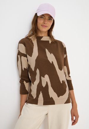 Braun und beige gemusterter Sweatshirt mit gerippter Textur, weitem Ausschnitt und langen Ärmeln, kombiniert mit einer hellrosa Mütze.