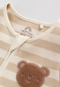 Body bébé à rayures beige doux et crème avec une applique en forme de visage d'ours brun duveteux sur la poitrine et une fermeture éclair à l'avant.