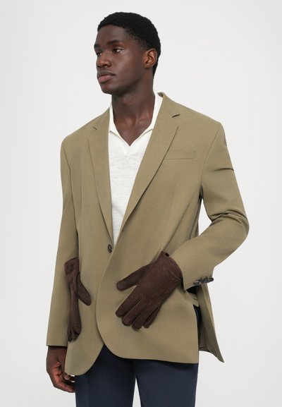 Olivgrüner Blazer mit einem einzelnen Knopf, der braune Wildlederhandschuhe enthält, die in die Taschen gesteckt sind. Weicher Stoff, taillierte Passform mit strukturierten Schultern.