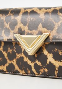 Leopardmintás műbőr táska, hajtogatott fedéllel és arany háromszög alakú zárakkal. Texturált felülettel és fekete varrással rendelkezik.