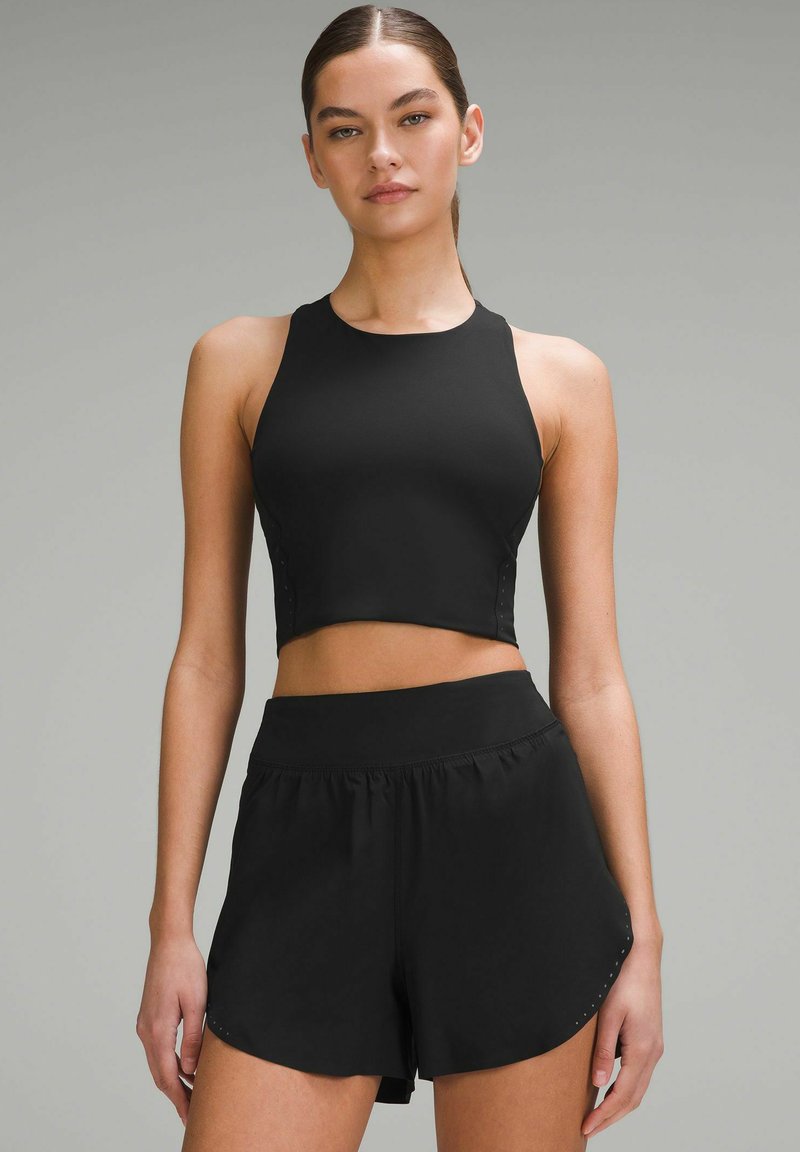 Čierny športový crop top s vysokým golierom, v kombinácii s čiernymi šortkami s širokým pásom a bočnými akcentmi.
