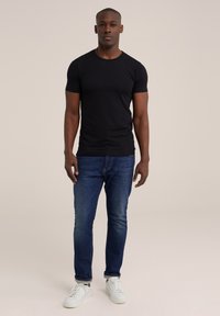 Camiseta negra de manga corta, cuello redondo, combinada con jeans azules y zapatillas blancas. La tela parece suave; el ajuste es ceñido y casual.