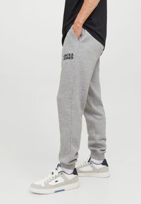 Grey joggers made of soft fabric with side pockets, featuring a logo print. Paired with white and gray sneakers with blue accents.