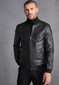Jachetă bomber din piele neagră, cu fermoar frontal, manșete ribbate și buzunare laterale. Textură netedă și design ajustat.