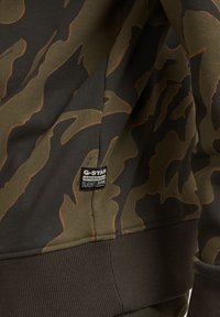 Sudadera con estampado de camuflaje en verde oscuro y marrón, con puños y dobladillo acanalados, y una etiqueta negra que muestra "G-Star Originals."