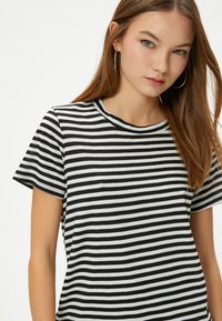 Camiseta de rayas en blanco y negro con cuello redondo y mangas cortas, hecha de una tela suave, con un corte holgado y sin logotipos visibles.