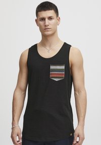 Tricou fără mâneci de culoare neagră, având un buzunar cu un model geometric în nuanțe de verde, roșu și albastru. Fabricat dintr-un material moale și ușor.