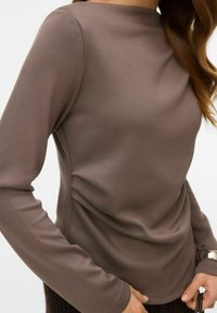 Brązowa bluzka z długim rękawem o dopasowanym kroju, gładkiej fakturze i okrągłym dekolcie. Materiał ma subtelny połysk i jest lekki.
