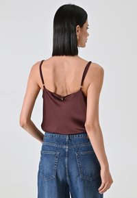 Burgunderfarbene Satin-Camisole mit dünnen Trägern, versehen mit einem Knopfdetail am Rücken, kombiniert mit hoch sitzenden blauen Denim-Jeans.