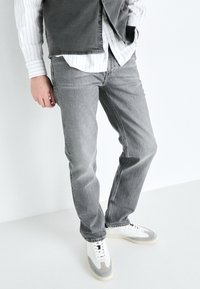 Jean en denim gris avec une coupe droite, featuring des poches avant, une texture légèrement délavée, associés à des baskets blanches et grises.