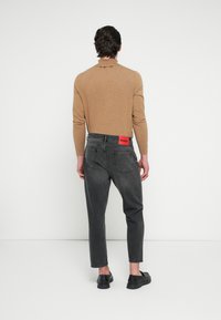 Grijze denim jeans met een rechtlijnig ontwerp en een rood merketiket aan de achterkant, gecombineerd met een lichtbruine top met lange mouwen.